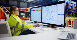 Worker monitoring logistics map on dual screens