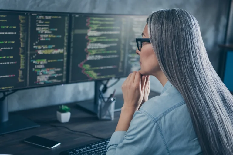 Female software engineer writing code on monitors