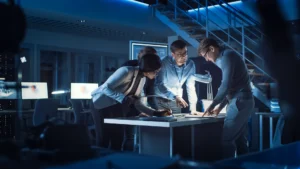 Three professionals reviewing documents on a illuminated table in a dark office