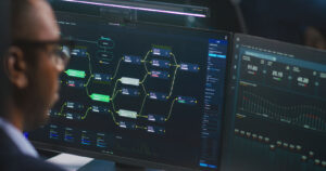 Professional monitoring a complex network flow diagram on dual screens in a dark environment