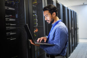 IT engineer using a laptop while managing servers in a data center