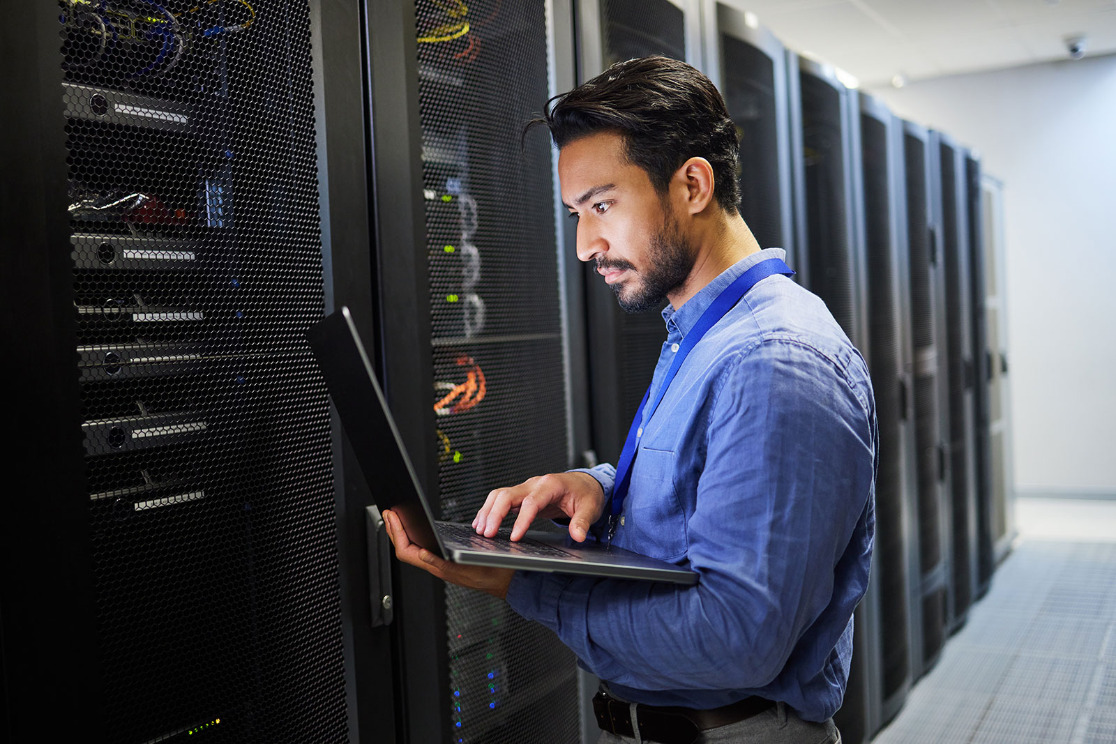 IT engineer using a laptop while managing servers in a data center