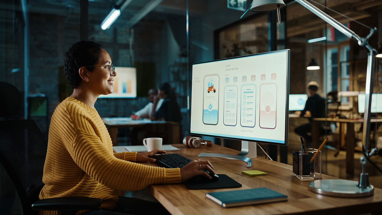 Designer reviewing mobile UI wireframes on desktop monitor in office