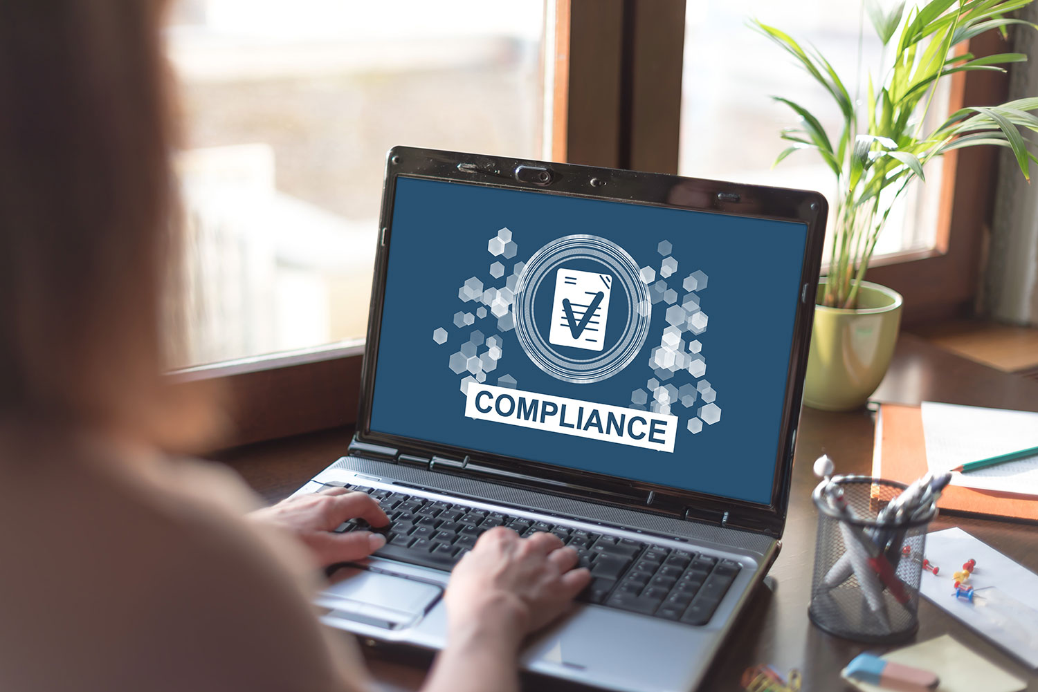 Person working on a laptop displaying a compliance concept graphic