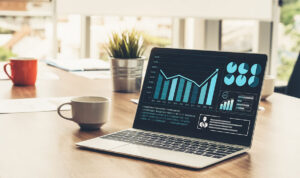 Laptop displaying a business analytics dashboard with bar charts on a wooden desk