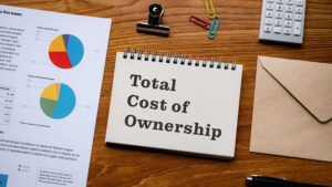 Notebook labeled total cost of ownership with financial charts on a wooden desk