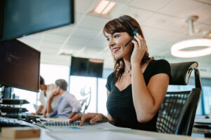 Woman smiling while wearing a headset and working at a computer in an office