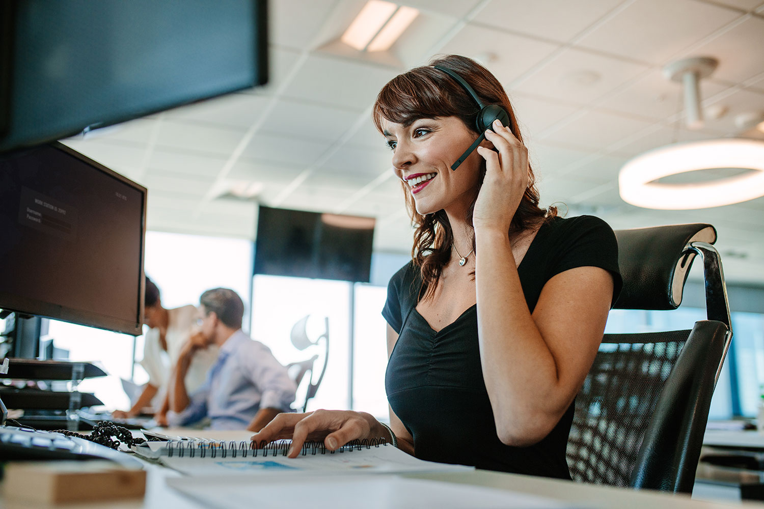 Woman smiling while wearing a headset and working at a computer in an office