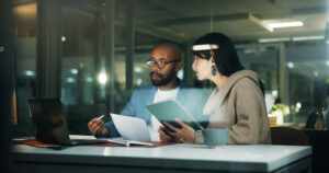 Two colleagues reviewing documents and a notebook together in a dimly lit office