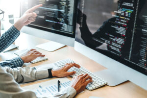 Two developers typing and pointing at code on large desktop monitors