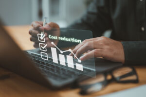 Hands on a laptop with a glowing cost reduction chart and checklist overlay