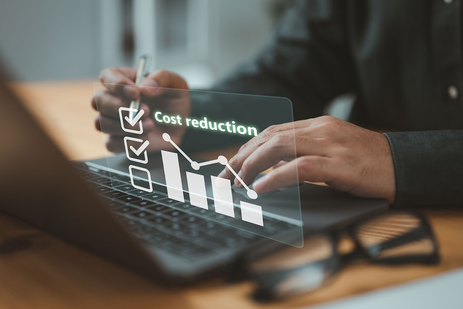 Hands on a laptop with a glowing cost reduction chart and checklist overlay