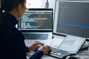 Developer coding on a laptop with a large external monitor displaying code
