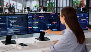 Woman pointing at a network dashboard across multiple monitors in an office