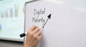 Person drawing an upward arrow beside digital maturity text on a whiteboard