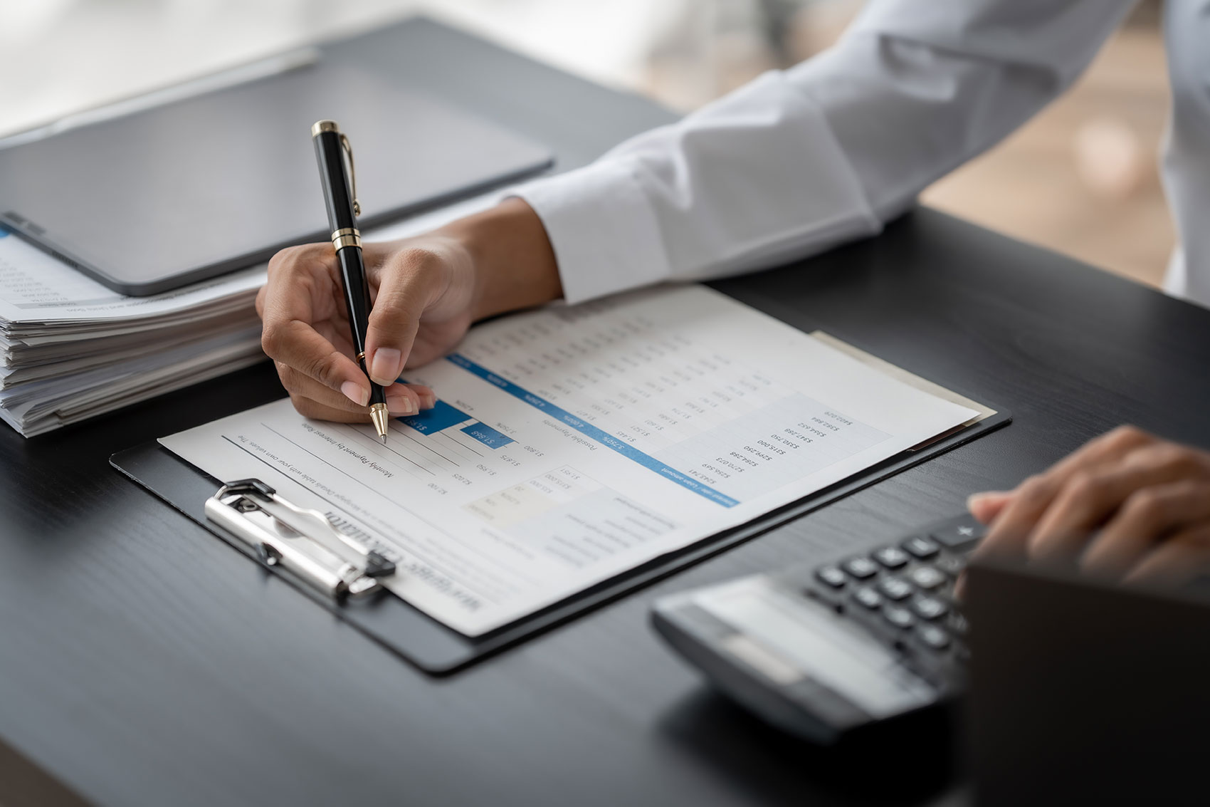 Professional writing on ERP report clipboard with calculator and laptop on desk