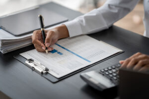 Professional reviewing ERP report on clipboard with calculator and laptop on desk