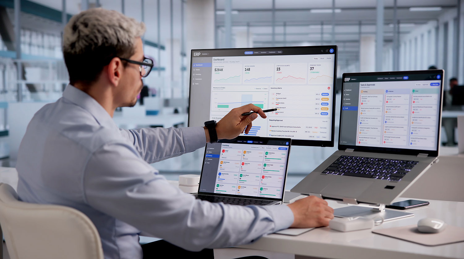 Professional pointing at a dashboard on a large monitor with two laptops on a desk