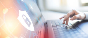 Hand on a laptop keyboard with a glowing cybersecurity shield and lock icon overlay