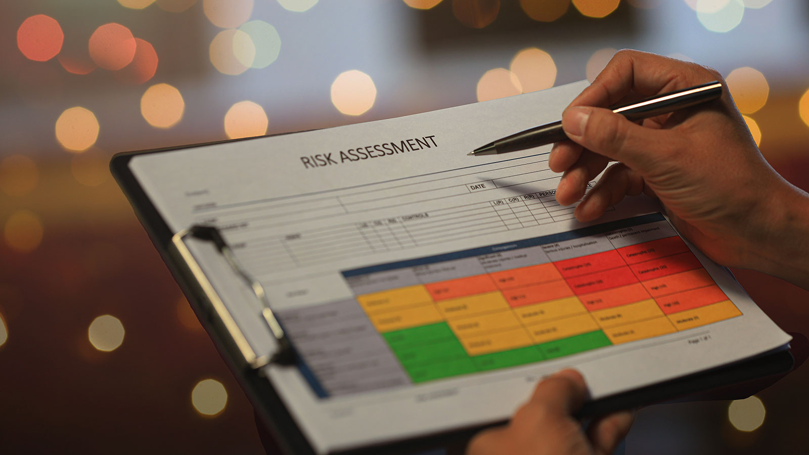 Hand filling out a risk assessment form with color-coded matrix on clipboard