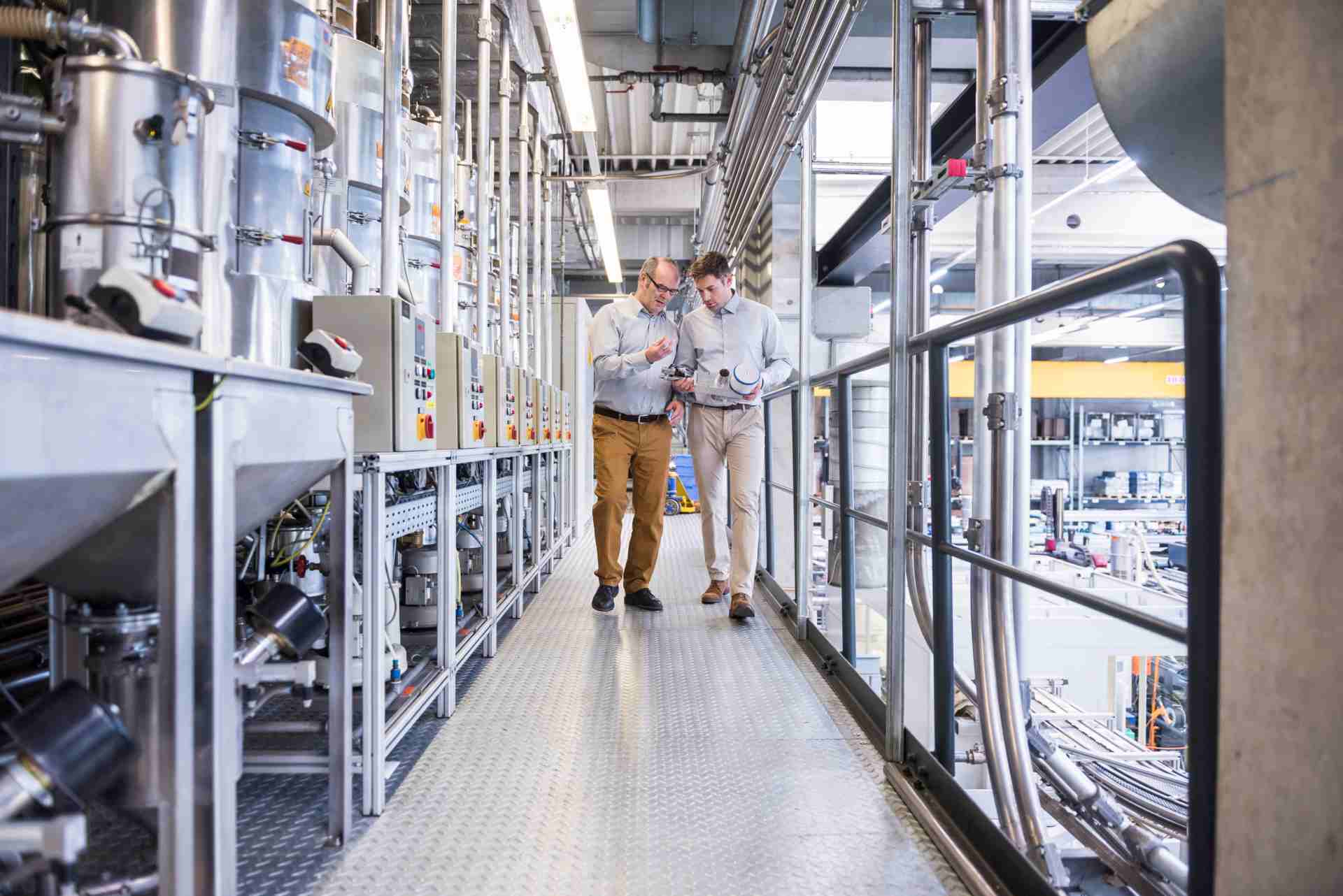 Two engineers reviewing a tablet while walking through an industrial facility