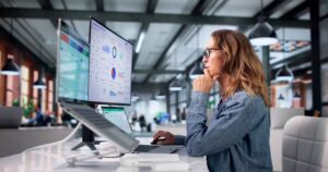 Person analyzing dashboard charts on dual monitors at office desk