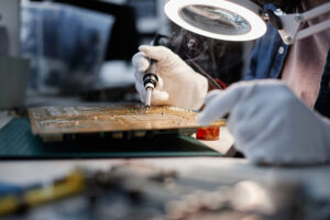 Technician soldering a circuit board under a magnifying lamp