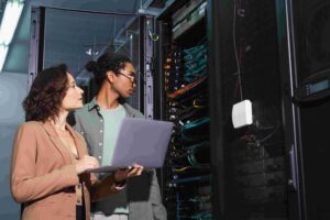 IT specialists examining rack-mounted devices with laptop in hand